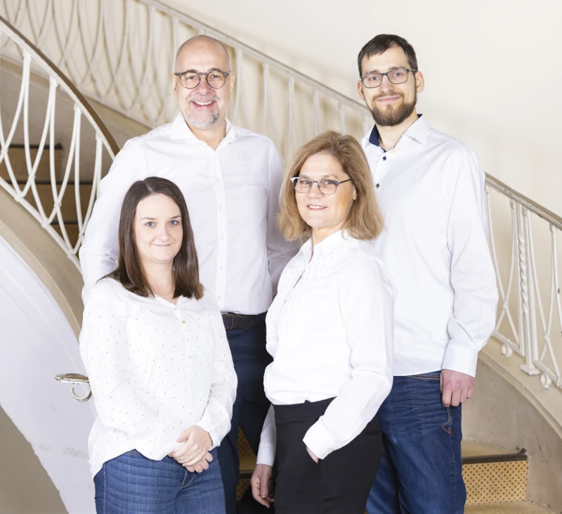 Vierköpfiges Team in weißer Kleidung posiert lächelnd vor eleganter Treppe im Büro.